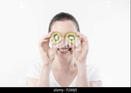 Mature woman holding kiwi slices in front of her eyes, Bavaria, Germany Stock Photo