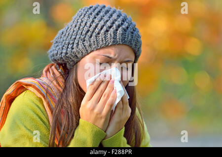 Girl in fall autumn park sneezing in tissue. Stock Photo