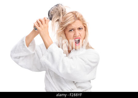 Displeased girl in a white bathrobe with her hair tangled in a hairbrush isolated on white background Stock Photo