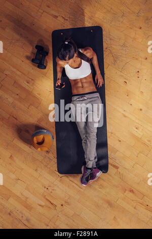 Top view of a young fitness woman relaxing on a yoga mat and using mobile phone. Female reading text message on her smart phone Stock Photo