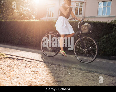 Cropped shot of woman riding bicycle along the street. Female cycling on road with sun flare. Stock Photo