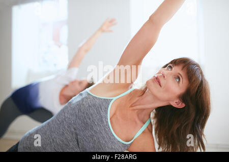 Portrait of mature woman practicing yoga at gym. Fitness female doing Triangle yoga Pose, Trikonasana. Stock Photo