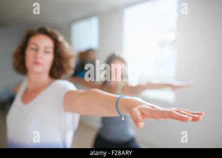 Fitness woman stretching her arms at yoga class. Young woman performing yoga in warrior pose. Virabhadrasana. Focus on hand. Stock Photo