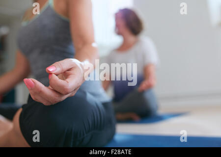Woman sitting with her legs crossed and hand resting on knee. Close up of meditating woman’s hand during yoga class. Lotus pose Stock Photo