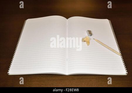 Opened notebook with sharpened pencil and pencil sharpener on wooden desk Stock Photo