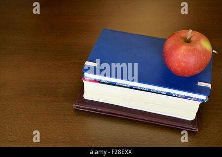 Pile of books, notebooks with red apple on brown wooden desk Stock Photo