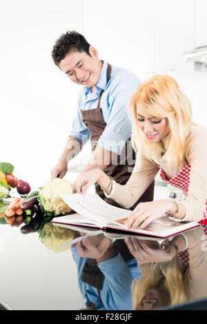 Asian couple reading recipes in cook book Stock Photo