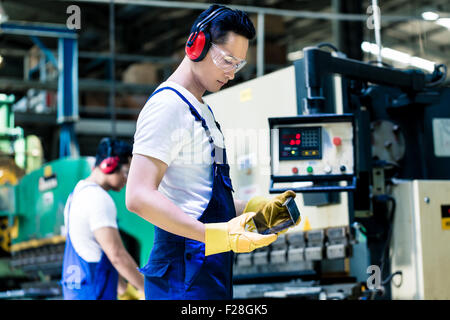 Asian machine operator in production plant checking data Stock Photo