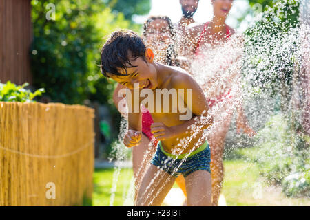 Family cooling down with sprinkler in garden, lots of water splashing around Stock Photo