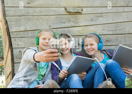 Three friends sitting in playground and listening music, Munich, Bavaria, Germany Stock Photo