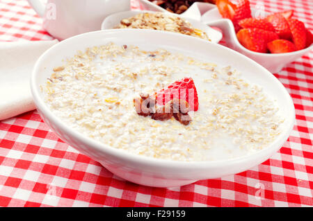 closeup of a bowl with porridge with sultana raisins and strawberry, on a set table with a checkered tablecloth for breakfast Stock Photo