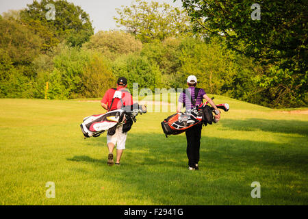 Two men carrying golf bags walk away across the course on a sunny, late spring afternoon in the golden light of the setting sun. Stock Photo