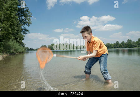 Boy catching fish with fishing net in the lake, Bavaria, Germany Stock Photo