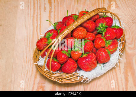 On the surface of the wooden table is a wicker basket filled with ripe red strawberries. Stock Photo