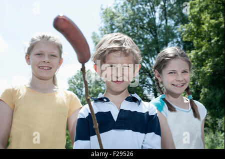 Three friends preparing sausage on campfire, Bavaria, Germany Stock Photo