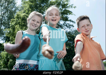 Three friends preparing sausages on campfire, Bavaria, Germany Stock Photo