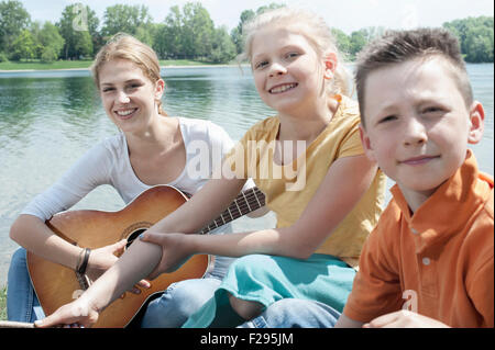 Young leader playing guitar with her friends at lakeside, Bavaria, Germany Stock Photo