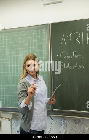 School teacher writing on blackboard in classroom, Munich, Bavaria, Germany Stock Photo