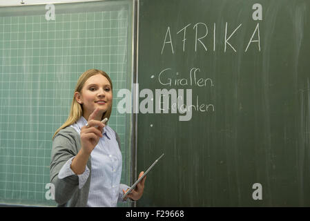 School teacher writing on blackboard in classroom, Munich, Bavaria, Germany Stock Photo