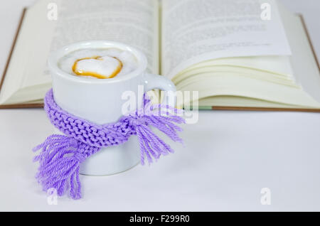 Purple winter knit scarf wrapped around cappuccino drink with heart and book on white.