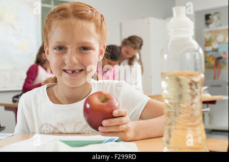 Portrait of a schoolgirl holding an apple in classroom, Munich, Bavaria, Germany