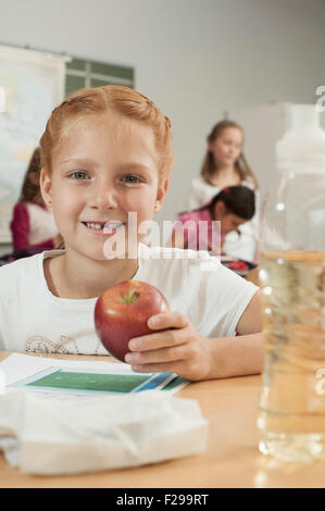 Portrait of a schoolgirl holding an apple in classroom, Munich, Bavaria, Germany