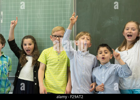 school students raising hands in front of blackboard in classroom, Munich, Bavaria, Germany, Stock Photo