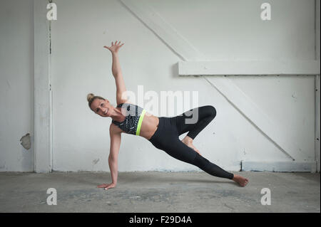Mid adult woman practicing side plank pose in yoga studio, Munich, Bavaria, Germany Stock Photo