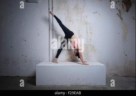 Mid adult woman practicing one legged downward facing dog position on concrete block, Munich, Bavaria, Germany Stock Photo