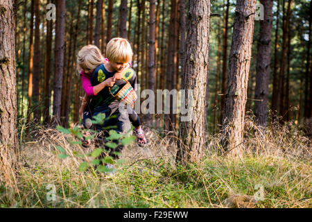 Young boy giving young girl piggyback outdoors smiling, forest, woodland, wood, summer, holiday, siblings, children playing, kid Stock Photo