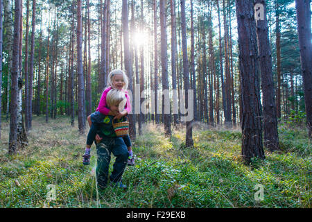 Young boy giving young girl piggyback outdoors smiling, forest, woodland, wood, summer, holiday, siblings, children playing, kid Stock Photo