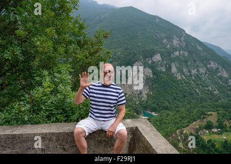 Portrait of mature man that is sitting with greeting gesture at viewing point near actor Bulatovic-Dzambas monument above Devil’ Stock Photo