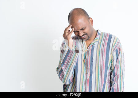 Portrait of Indian mature man having headache, hand rubbing forehead, standing on grey background. Stock Photo