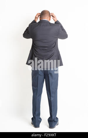 Rear view full body mature Indian business man hands scratching head and running out of idea , standing on plain background. Stock Photo