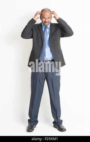 Full body mature Indian business man hands scratching his bald head , standing on plain background. Stock Photo