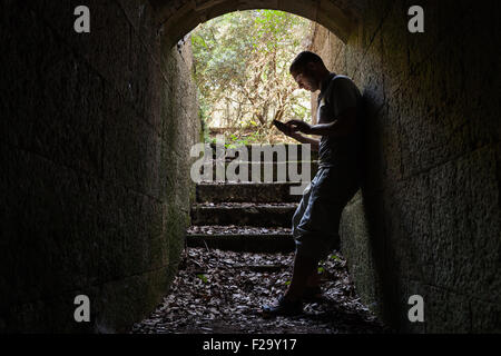 Young man works on a smart-phone in dark stone tunnel Stock Photo