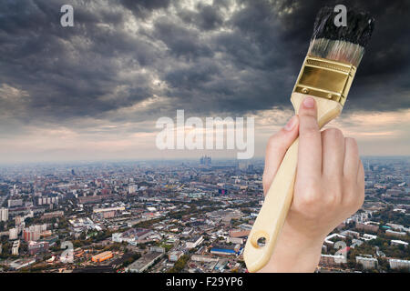 nature concept - hand with paintbrush paints storm clouds over dark city Stock Photo