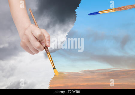 nature concept - seasons and weather changing: hand with paintbrush paints sunset sky instead of rainy clouds Stock Photo