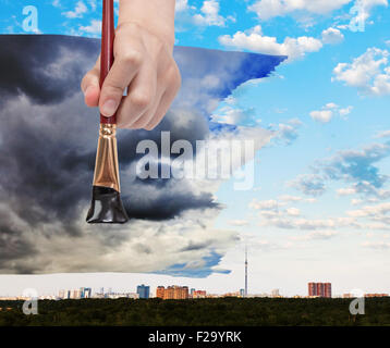 nature concept - seasons and weather changing: hand with paintbrush paints black storm clouds over city Stock Photo