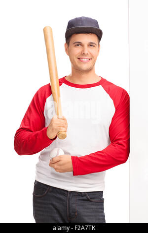 Vertical shot of a young man holding a baseball bat and leaning against a wall isolated on white background Stock Photo