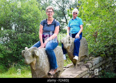 Two women sitting on stone sheep sculptures by Keith Alexander. On the Pennine Way at Low Force, Teesdale, England. Stock Photo