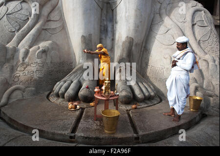 A jaïn pilgrim ( the man dressed in orange) is worshipping Gomateshwara, one of the main jaïn spiritual leader ( India) Stock Photo