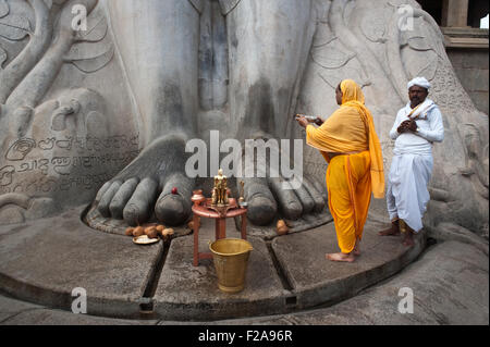 A jaïn pilgrim ( the man dressed in orange) is worshipping Gomateshwara, one of the main jaïn spiritual leader ( India) Stock Photo