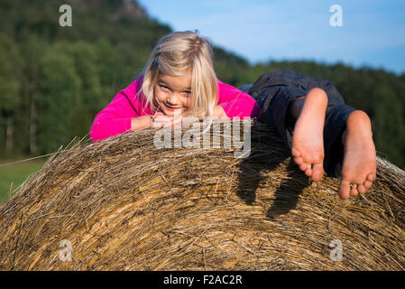 Children blond girl and boy (siblings) resting on hay bale, summer, holiday, relaxing Stock Photo