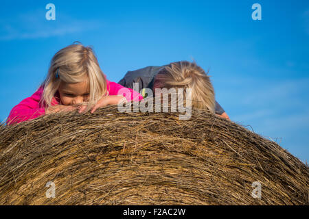 Children blond girl and boy (siblings) resting on hay bale, summer, holiday, relaxing Stock Photo