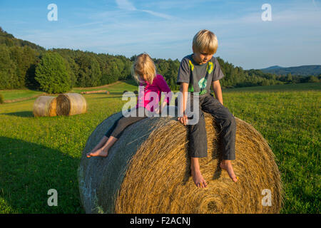 Children blond girl and boy (siblings) resting on hay bale, summer, holiday, relaxing Stock Photo