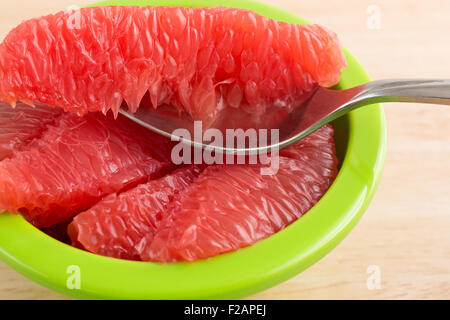 Close view of sections of red grapefruit in a green bowl with a spoon on a wood table top. Stock Photo