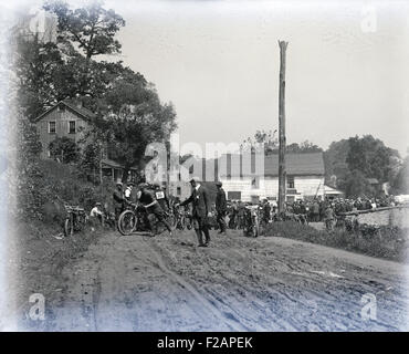 Antique circa 1910 photograph, participants in an early motorcycle race, in a small town with muddy roads. Location, USA. Stock Photo