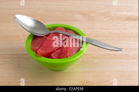 Sections of red grapefruit in a green bowl with a spoon on a wood table top. Stock Photo