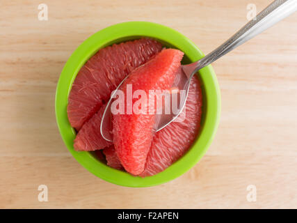 Top view of sections of red grapefruit in a green bowl with a spoon on a wood table top. Stock Photo